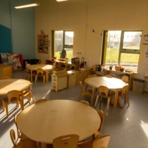 Bright classroom with multiple wooden tables and chairs.